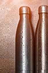 Stainless thermo bottles, on a wooden table sprayed with water.