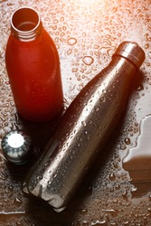 Two stainless thermo bottles on a wooden table sprayed with water. With sunlight effect.