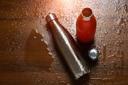 Two stainless thermo bottles on a wooden table sprayed with water. With sunlight effect.