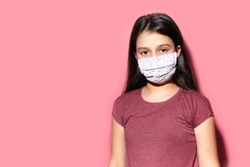 Studio portrait of teenage girl wearing medical face mask against coronavirus. Prevention of covid-19. Background of pastel pink color with copy space.