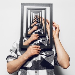 Enigmatic surrealistic optical illusion. Man holding black picture frame.