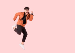 Happy handsome Asian man in fashionable clothing and jumping doing winner gesture isolated on pink background with clipping path. Portrait of young male cheerful jumping in air and smiling in studio.