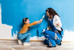 Mother and daughter enjoying together while painting wall.