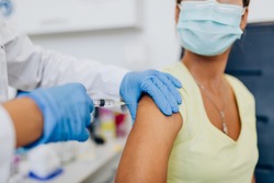 Female doctor or nurse giving shot or vaccine to a patient's shoulder. Vaccination and prevention against flu or virus pandemic. 
