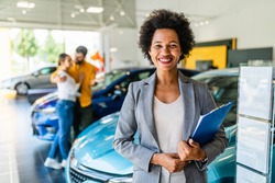 African American saleswoman working at car showroom. Customers in the background. 