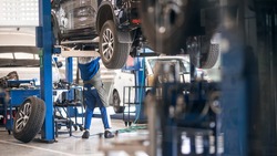 Mechanic inspecting car suspension detail and wheel car of lifted automobile at repair service station. Car service station. Preventive maintenance.
