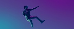 Young Asian man wearing VR headset playing video game and levitating in the air on futuristic purple cyberpunk neon light banner background. Metaverse technology concept.