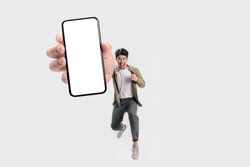 Full length of cheerfull Asian man jumping and smiling in air with showing cellphone blank screen with empty space for mobile app on screen. Isolated in studio white background. Creative collage.
