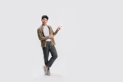 Full length smart young Asian man happy smile standing hand pointing to empty space on white background. Short on studio.
