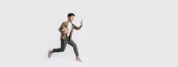 Full length handsome Asian man holding box and use smartphone he is run and jumping in air on banner white background. Young male happy excited and using mobile phone with shopping online concept.