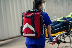 Selective focus, Medical bag on back of paramedic female during move worker is patient lying on ambulance stretcher into emergency car for transfer to hospital. Emergency worker accident at workplace.