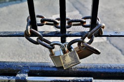 Lock on chain. A chained gate or fence with a heavy chain and three silver and bronze colored locks or padlocks.