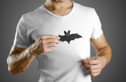 A man in a white t-shirt holds a black silhouette of a bat. Close up.