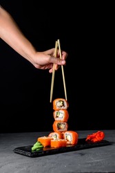 Set of Philadelphia or California sushi on black stone slate. Over grey, over gray background. Japanese cuisine concept. Creative advertisement concept, vertical banner. Eating sushi with chopsticks.