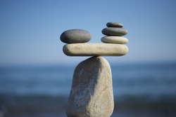 Stones pile background. Scales balance. Balanced stones on the top of boulder. To weight pros and cons. Balance of stones on a blue sky background with a copy space.