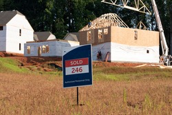 A SOLD sign is displayed in front on a lot with new houses being constructed in the background. 