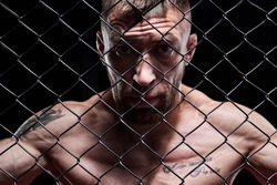Portrait of a powerful fighter behind the steel bars of the octagon. The concept of sports, Muay Thai, martial arts.