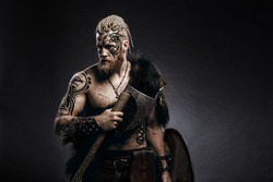 Medieval warrior berserk Viking with tattoo on skin, red beard and braids in hair with axe and shield attacks enemy. Concept historical photo