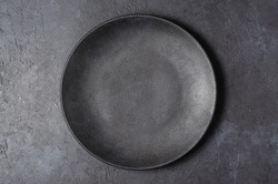 Dark grey textured concrete background for design with black food plate. Copy space