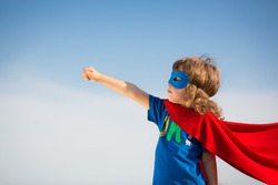 Superhero kid against blue sky background. Girl power concept