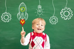 Bright idea! Funny child student pointing finger up! Happy kid against green chalkboard. Online education and e-learning concept. Back to school