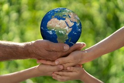 Family holding 3D planet in hands against green blurred background. Earth day spring holiday concept. Elements of this image furnished by NASA