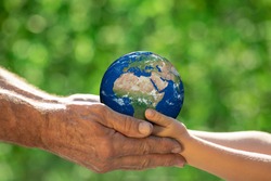 Family holding 3D planet in hands against green blurred background. Earth day spring holiday concept. Elements of this image furnished by NASA