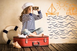 Happy kid playing with toy sailing boat indoors. Travel and adventure concept