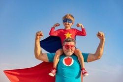 Superhero senior man and child playing outdoor. Super hero grandfather and boy having fun together against blue summer sky background. Family holiday concept. Happy Father's day