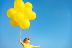 Happy child playing with yellow balloons outdoor. Kid having fun against blue summer sky background. Freedom and active lifestyle concept