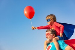 Superhero senior man and child playing outdoor. Super hero grandfather and boy having fun together against blue summer sky background. Family holiday concept. Happy Father's day