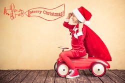 Child riding in red car. Kid holding Christmas bag. Xmas holiday concept