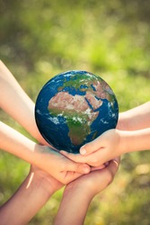 Children holding blue planet in hands against green spring background. Earth day holiday concept. Elements of this image furnished by NASA