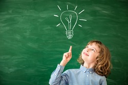 Back to school concept. School child in class. Smart kid against green blackboard. Schoolchild drawing light bulb on chalkboard. Idea and creativity concept. Copy space for your text