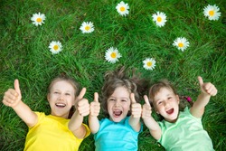 Group of happy children playing outdoors. Kids having fun in spring park. Friends lying on green grass. Top view portrait