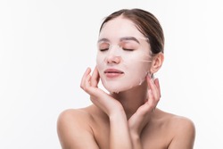Face care and beauty treatments. Woman with a cloth moisturizing mask on her face isolated on gray background