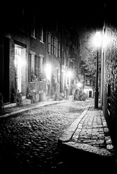 An old 19th Century cobble stone road in Boston Massachusetts, Lit only by the gas lamps revealing the shuttered windows and brightly lit doorways of the rowhouses on Acorn Street.
