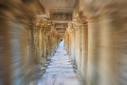 Viewed from the entrance, a zoom blur photo of ancient stone columns in a long temple passageway near Angkor Wat, Cambodia.