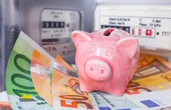 Pink piggy bank and Euro money near an electricity meter and gas meter. Utility bills, consumption of electricity and gas for heating home, energy costs, symbolic image.
