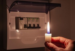 Housewife in complete darkness holding a candle to investigate a home fuse box during a power outage. Blackout, symbolic image.