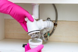 Long hair and grime are the cause of a clogged sink. Plumber in pink rubber gloves clearing a clogged very dirty drain at home.