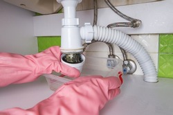 Person dressed in rubber protective gloves clearing a clogged very dirty drain at home. Long hair and grime are the cause of a clogged sink. 