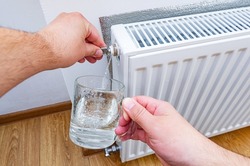 Hand with a key for draining drains water and air from the heater in a cup. Adjust heating system, preparing the house for the new cold autumn or winter season. Bleed valve in heating radiator.