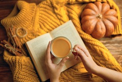 Vintage book with romantic stories and fairy tales. Top view of autumn composition with book and knitted sweater. Hot cocoa in hands, ripe pumpkin, warm sweater and open book on wooden background. 