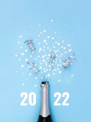 Open bottle of champagne on blue background decorated with silver star confetti and numbers 2022 . New Years celebration or party. Selective focus.