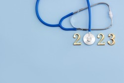 Stethoscope and metal numbers 2023 on blue background. New Year medical calendar. Copy space