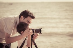 Dad is teaching son taking a photo at the beach at sunset with vintage color tone


