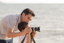 Dad is teaching son taking a photo at the beach at sunset
