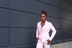 Stylish young african american girl wearing pink suit with bird brooch accessory. Female model wearing glamorous outfit. Stylish afro american woman posing outdoors. Concept of people and lifestyle.