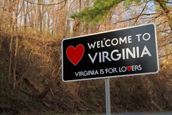 A roadside sign welcomes travelers along a rural road to the state of Virginia